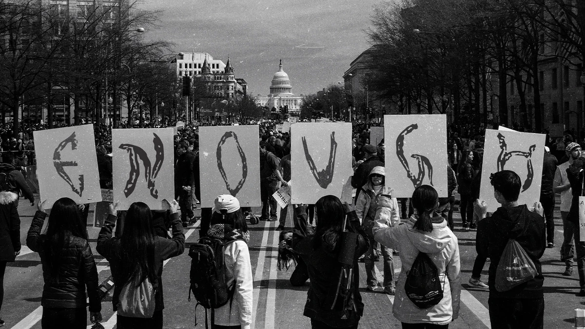 Protesters outside the Capitol holding placards that spell ENOUGH in the scar typeface.
