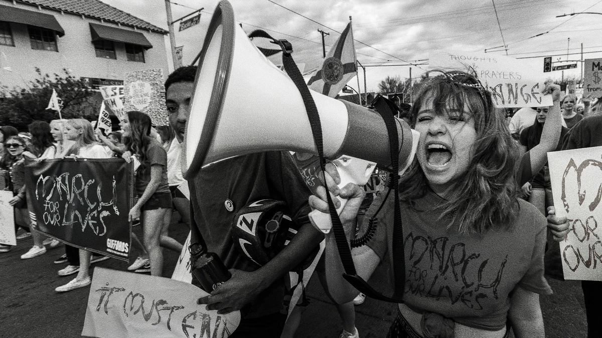 A protester shouting into a megaphone at a march, placards set in the scar typeface.
